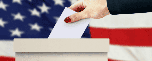 image of woman's hand putting vote into ballot box with American flag in background